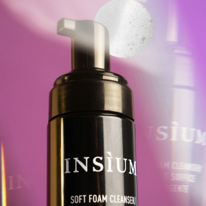Close-up of a black pump bottle labeled 'INSIUM' with 'Soft Foam Cleanser' on the label, set against a pink-purple background.